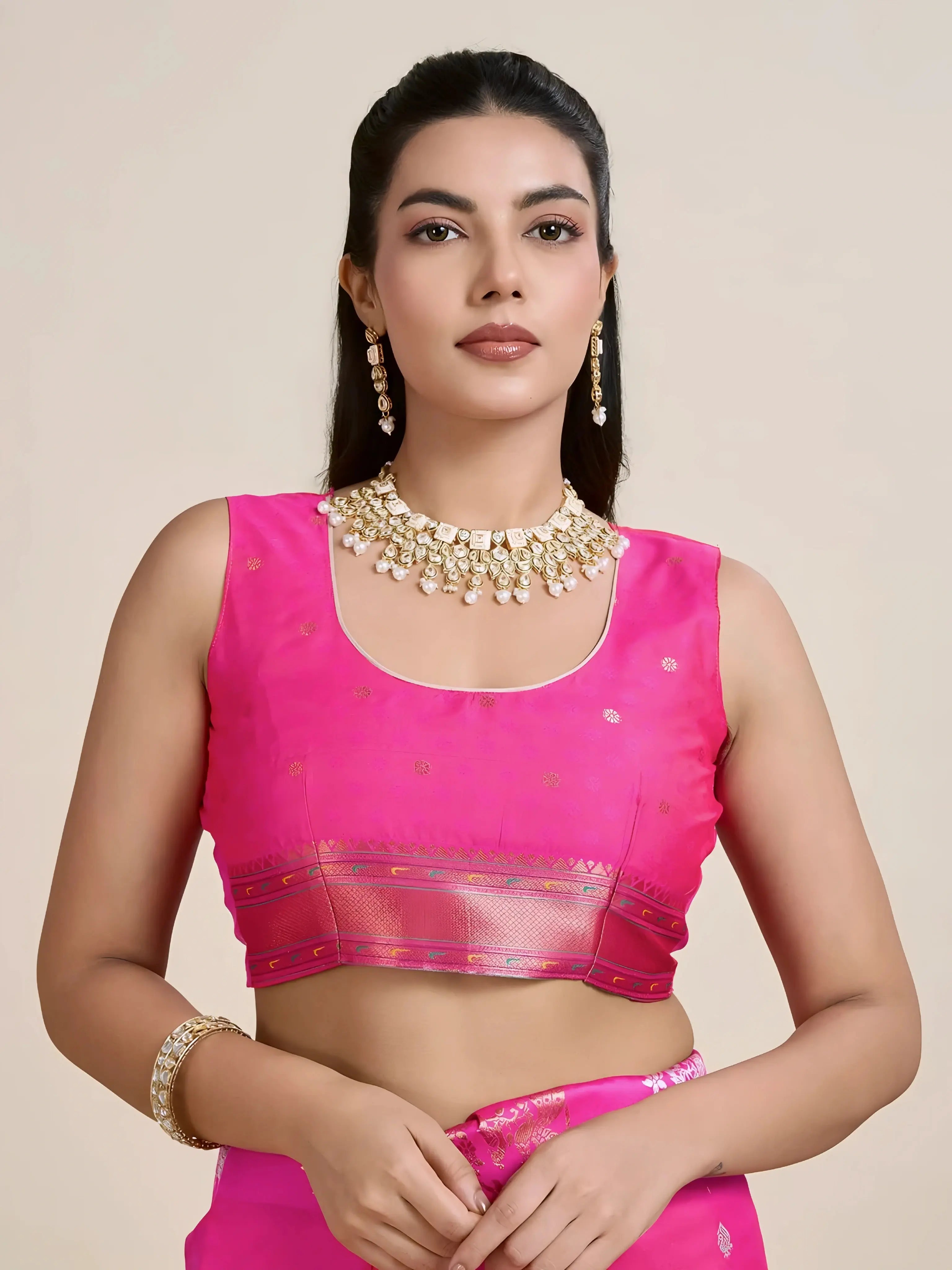 A woman models a luxurious Rani Pink Soft Silk Saree. The saree features scattered metallic motifs and a wide pallu in contrasting copper/rose gold, richly woven with multi-colored peacock and floral designs. She wears a matching pink sleeveless blouse and heavy gold Kundan jewelry, posing indoors.